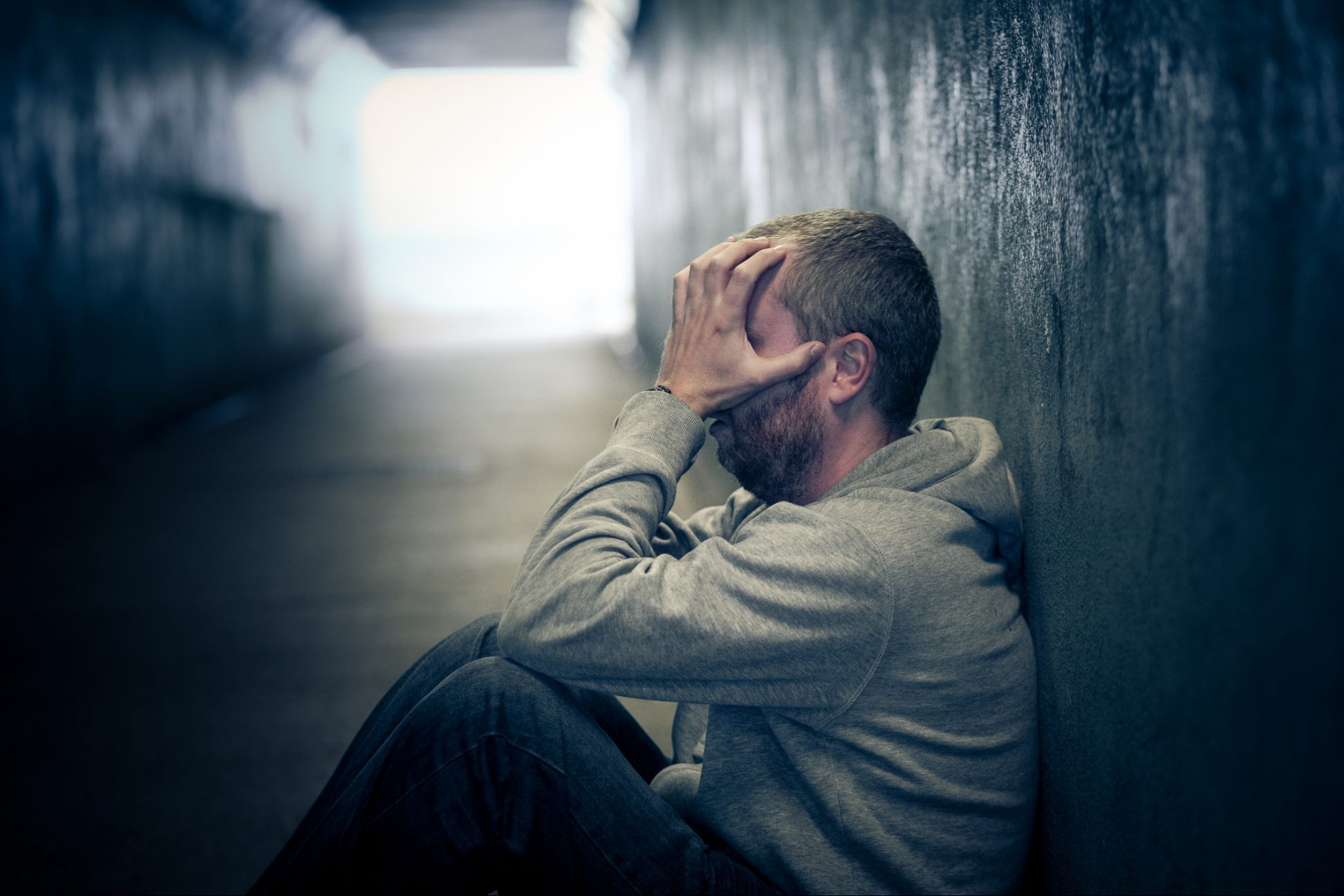 Young homeless caucasian male sitting in dark subway tunnel