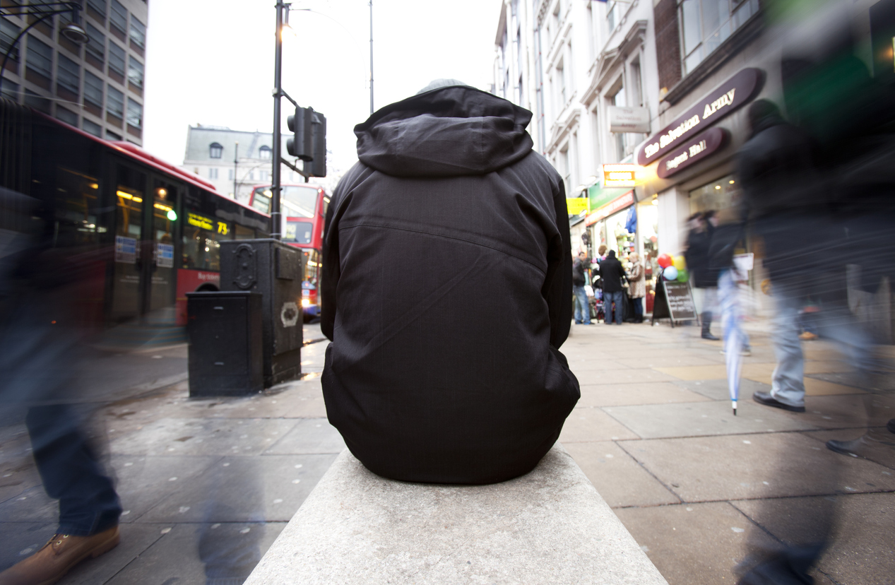 A homeless character sitting on a bench amidst the chaos of Christmas shoppers in the busy shopping district of London's Oxford Street, waiting for the homeless charity