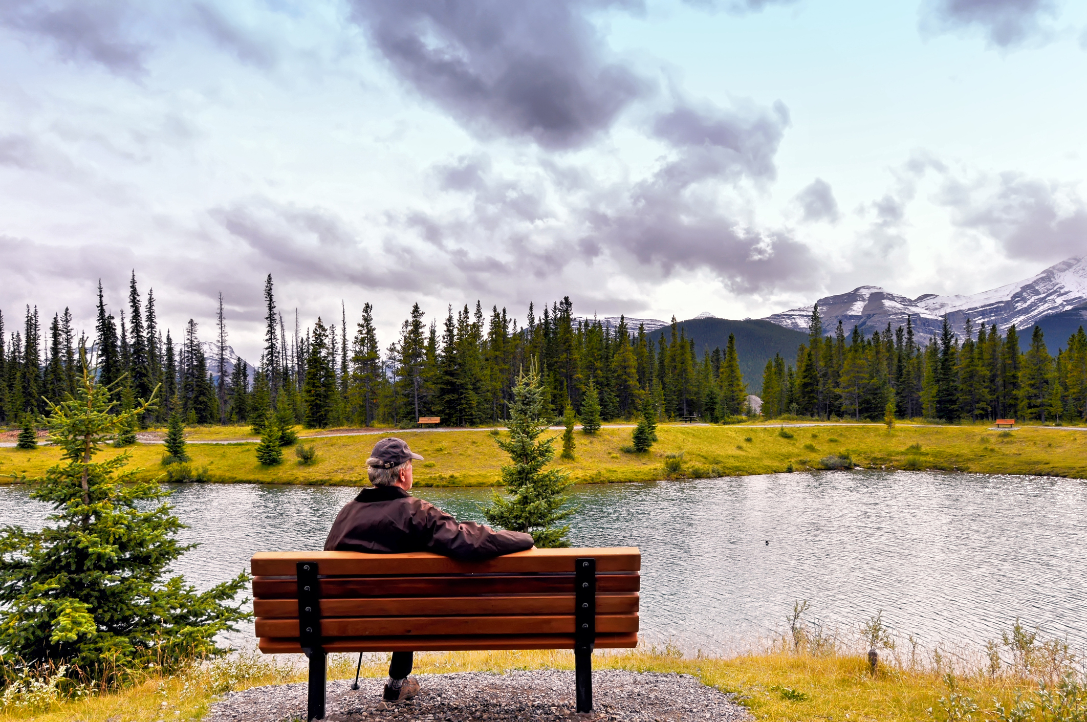 Caucasian senior man sitting on bench near the lake and admiring the landscape