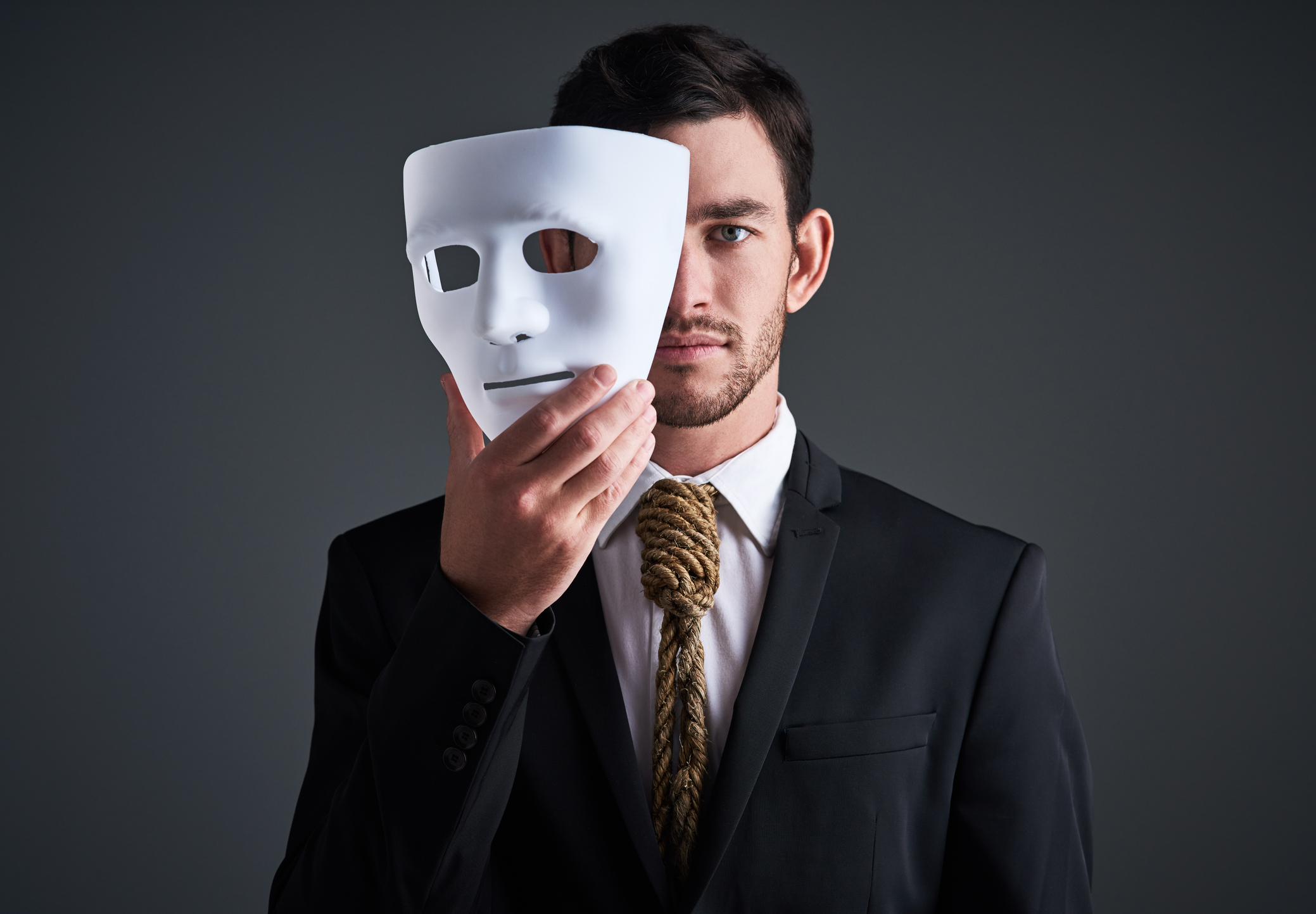 Studio portrait of a young businessman holding a mask in front of his face against a gray background