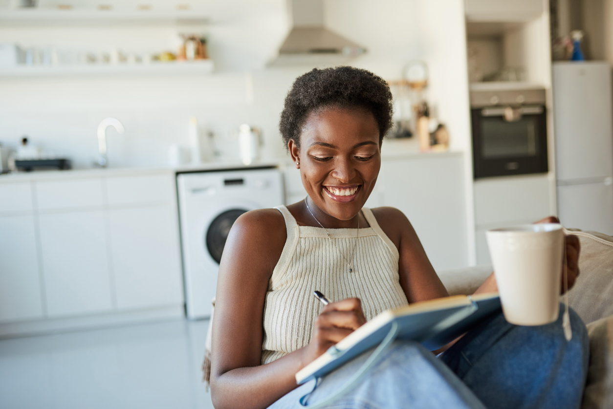 Shot of a young woman having tea and getting benefits from writing in a gratitude journal on the sofa at home