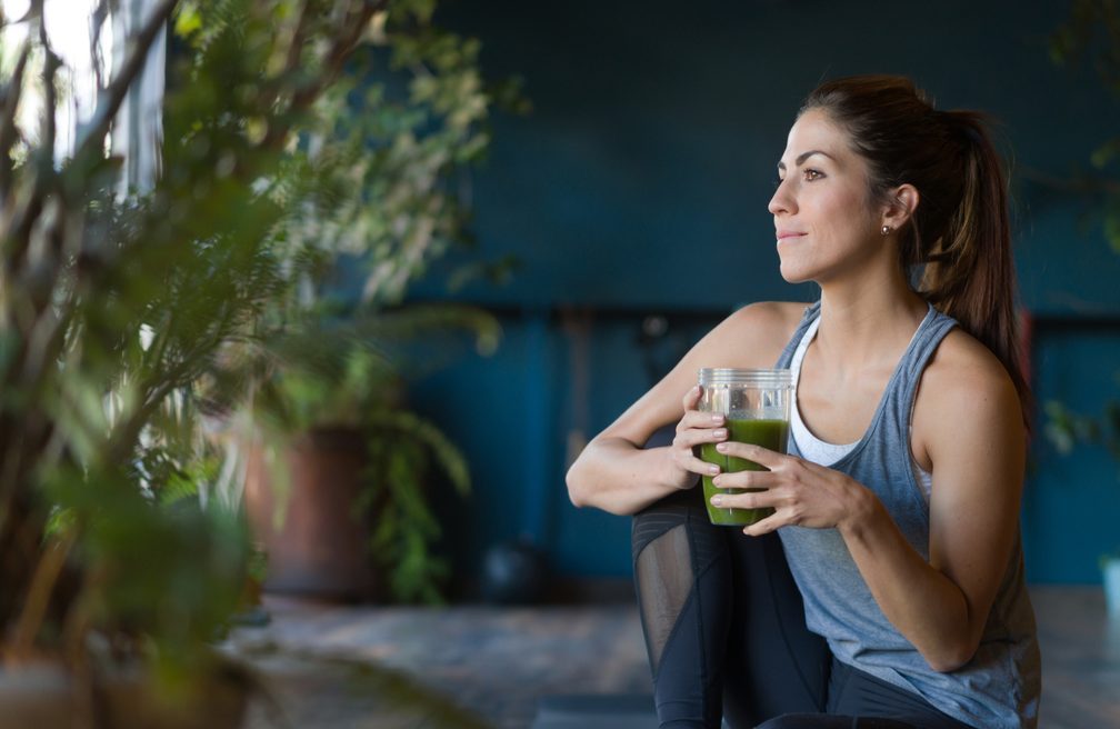 Fit woman drinking a green detox smoothie at the gym