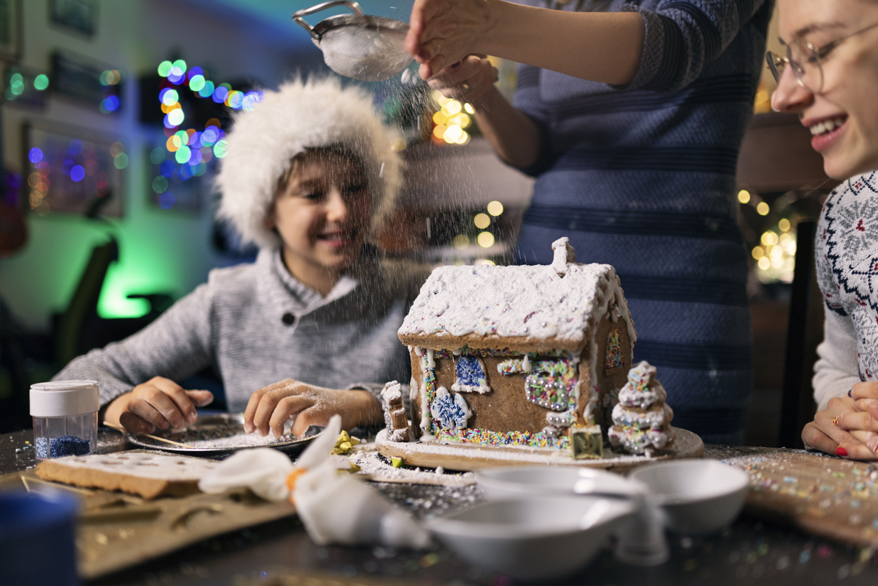Mother and kids enjoying building and decorating gingerbread house for Christmas