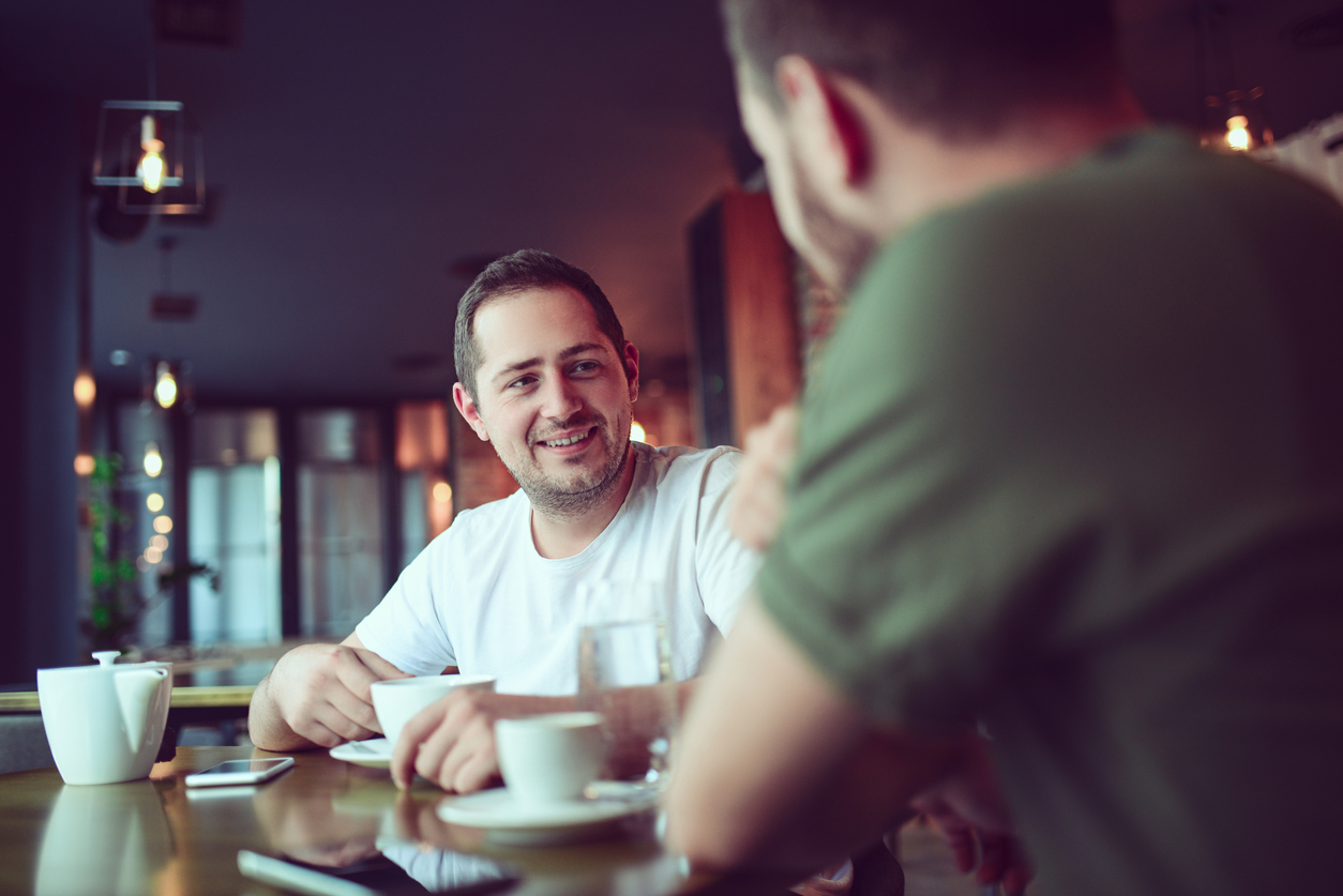 Two smiling handsome friend drinking coffee and socialising at favorite coffee place