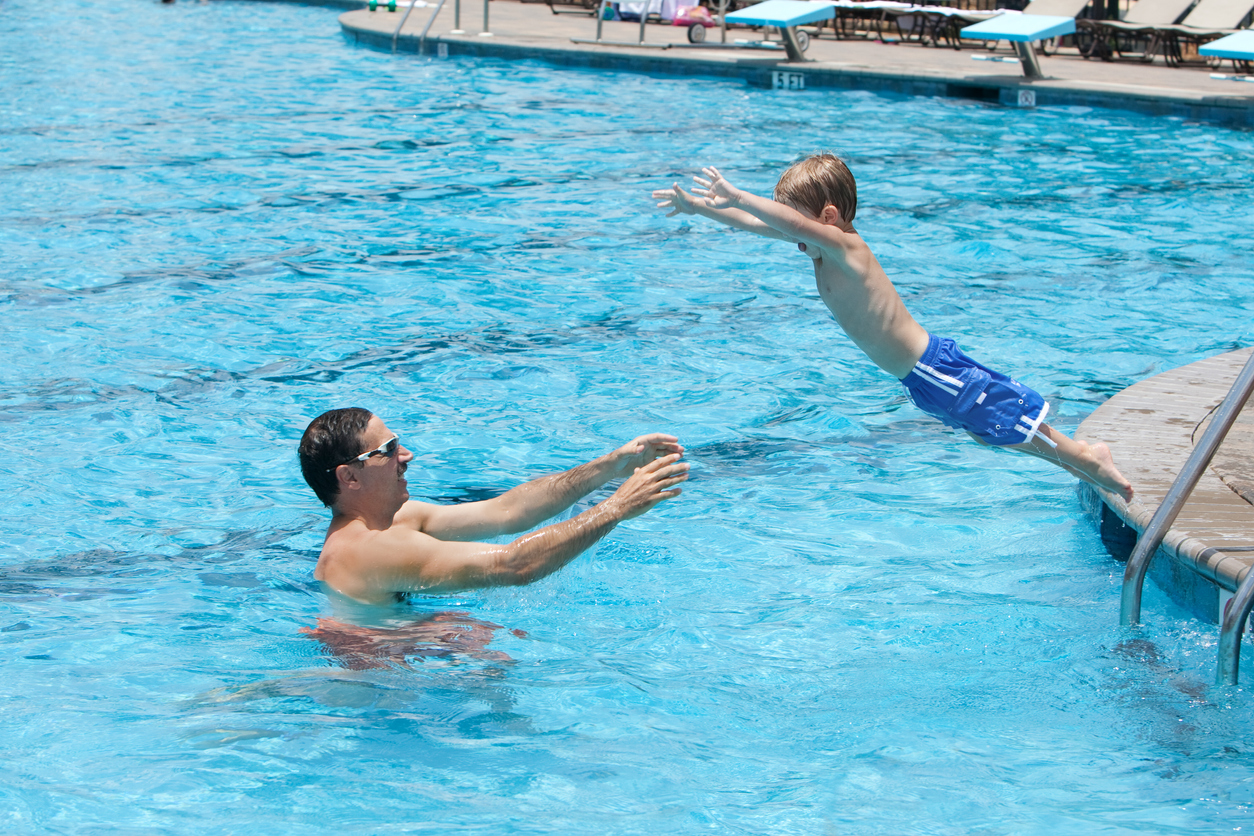 Little toddler, giving it all he's got as he jumps to his dad in the swimming pool