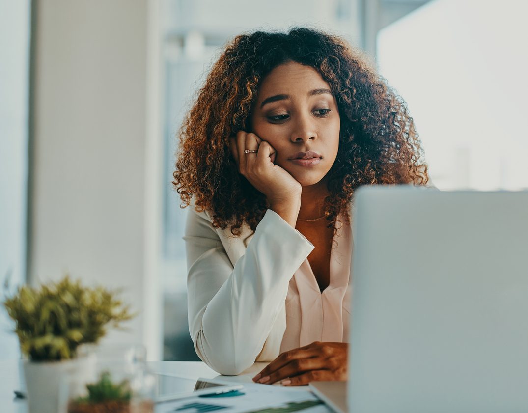 Shot of a young businesswoman looking bored and giving into procrastination while using a laptop in a modern office