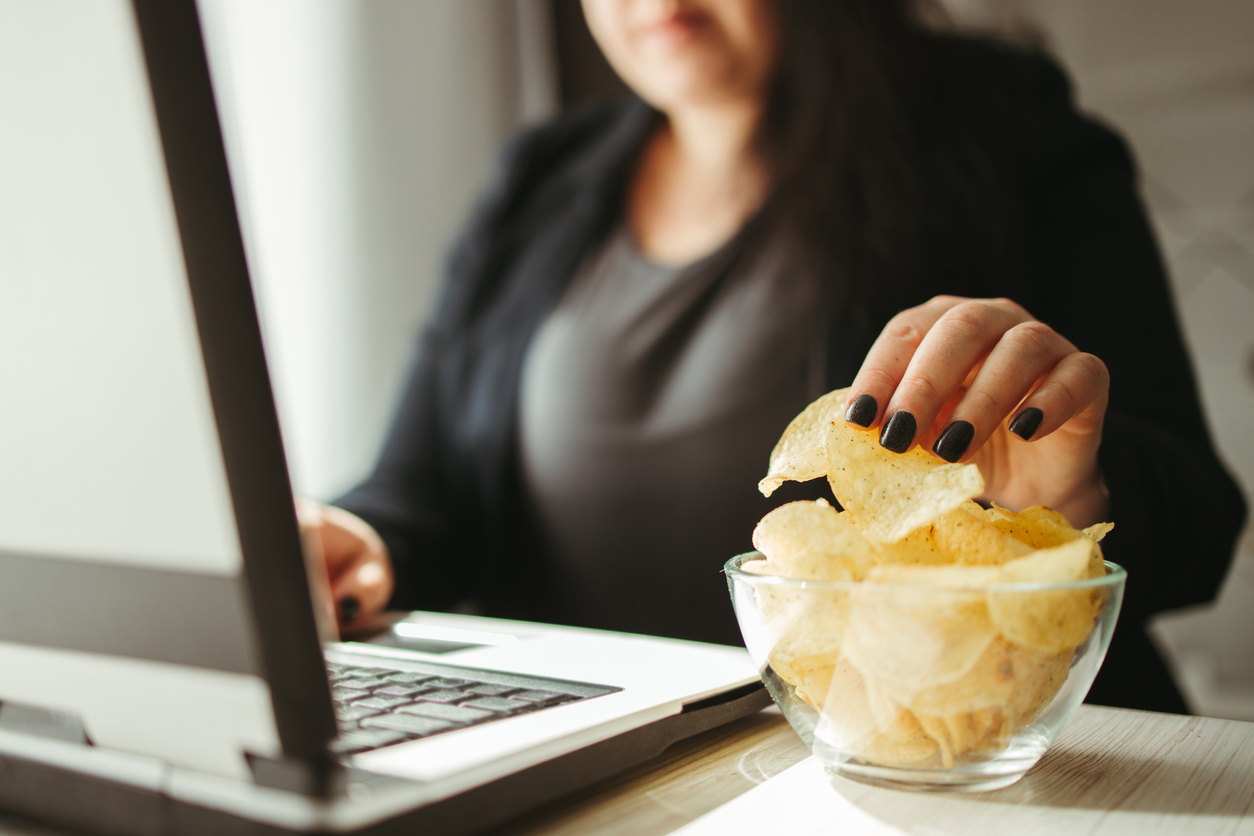 A woman reaching into a bowl of chips next to her laptop