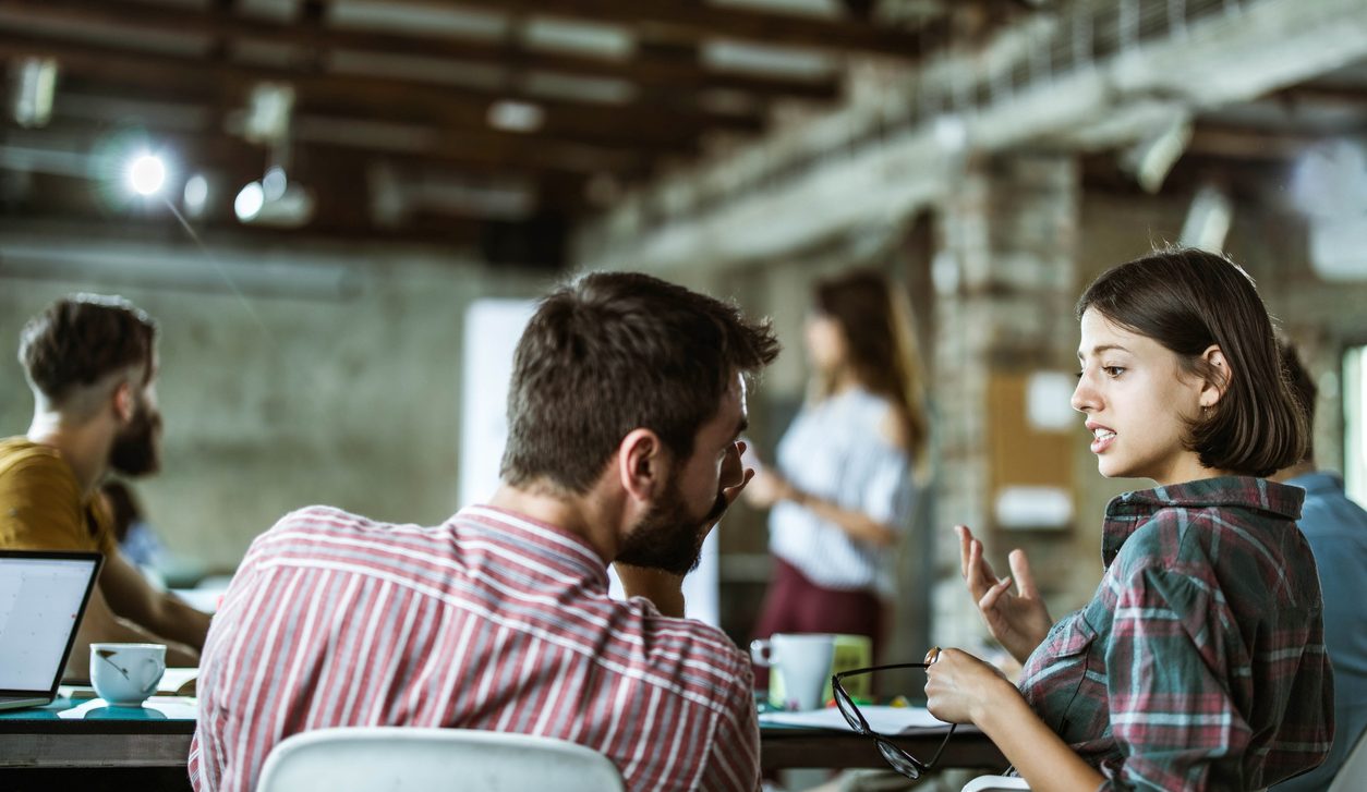 Creative couple talking gossip during a presentation in the office.
