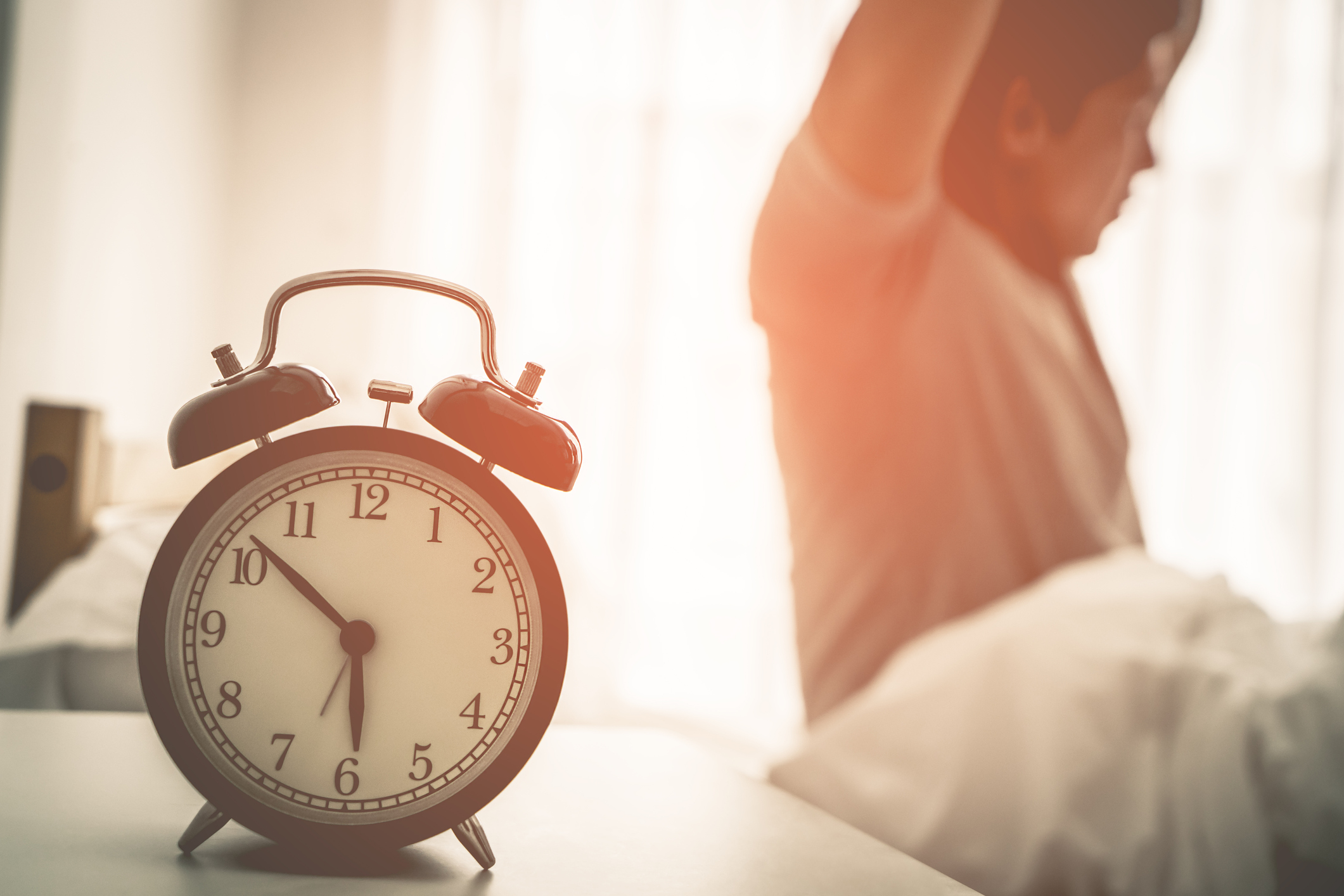 Asian male is stretching out after woke up with alarm clock showing six o clock