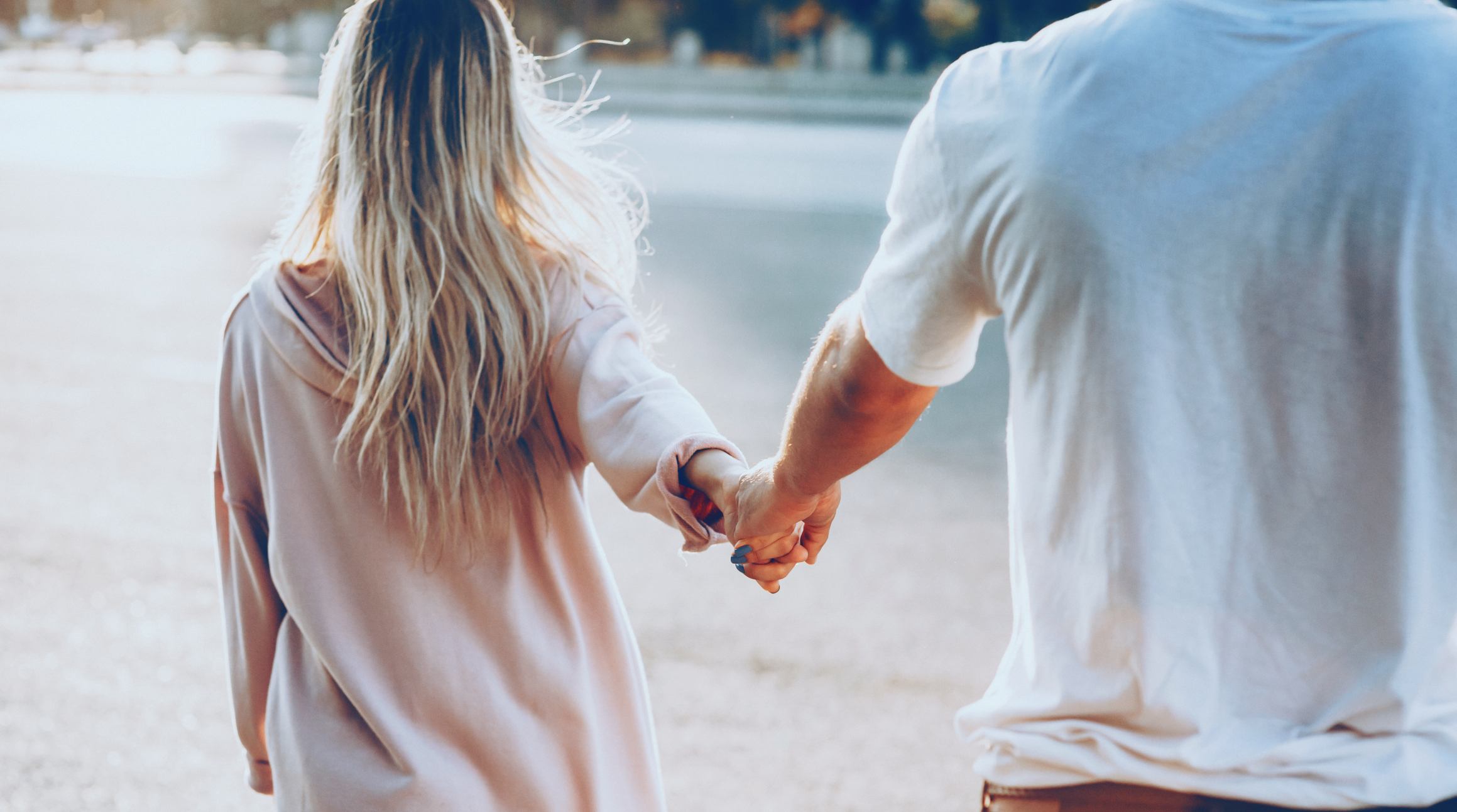 The back view of a young caucasian couple dressed in white walking hand in hand during sun is warming them