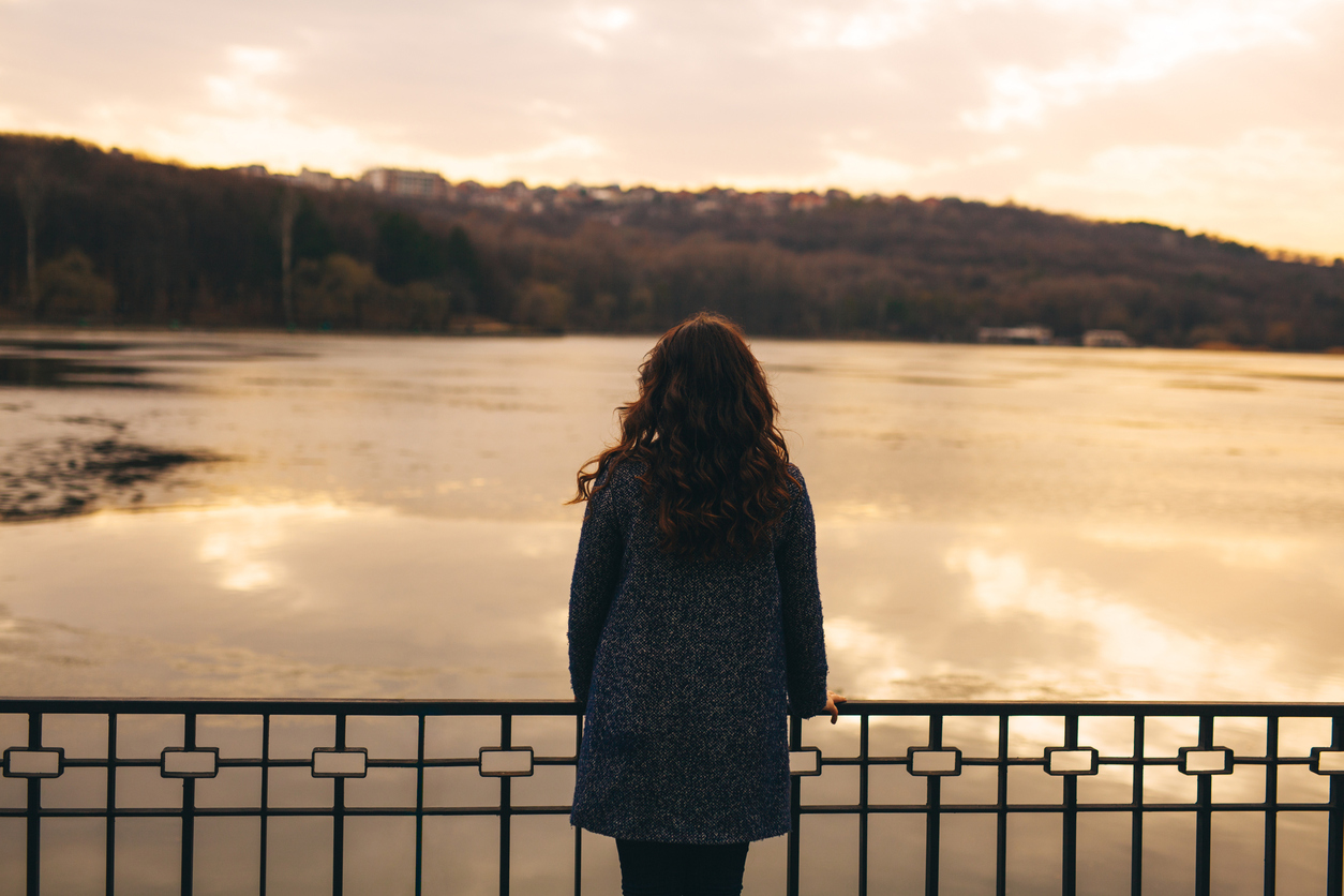 Rear view of sad woman silhouette at sunset lake