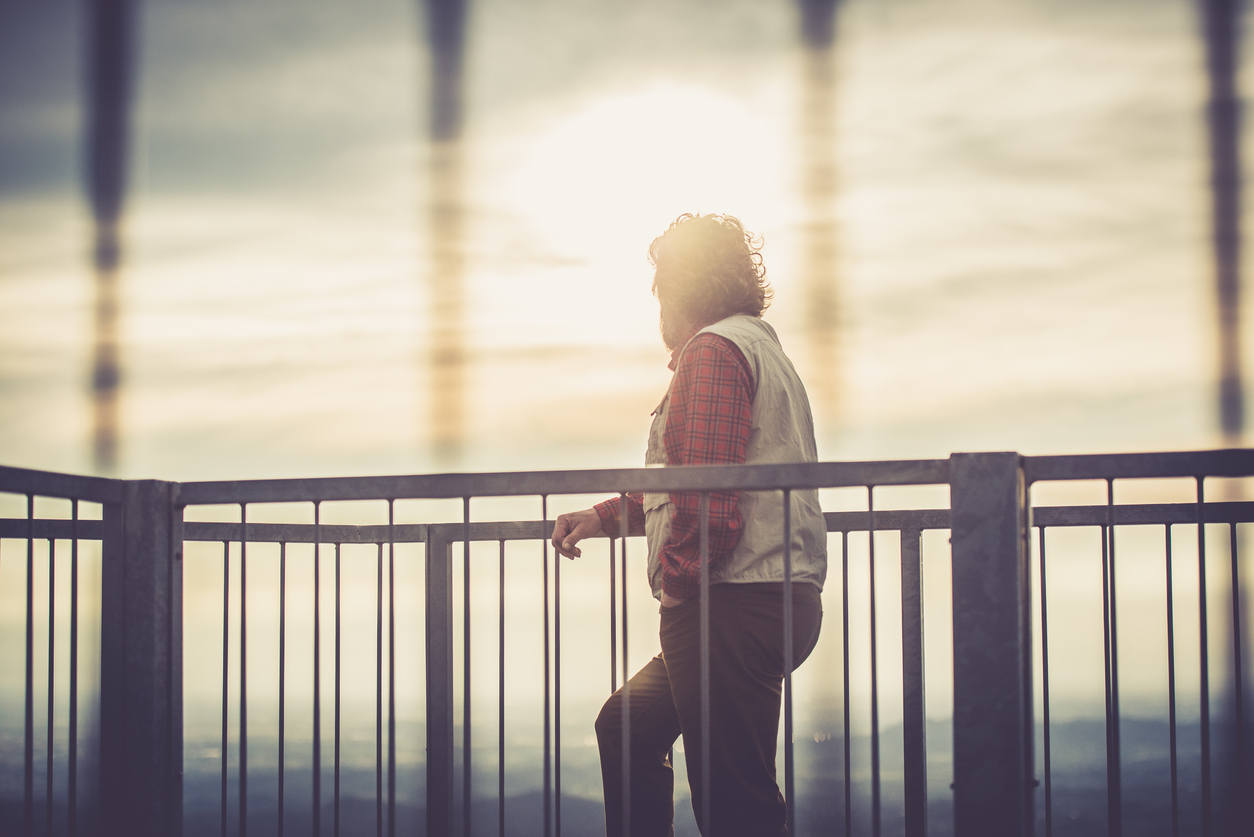 A man leaning against the railing stares at the sunset