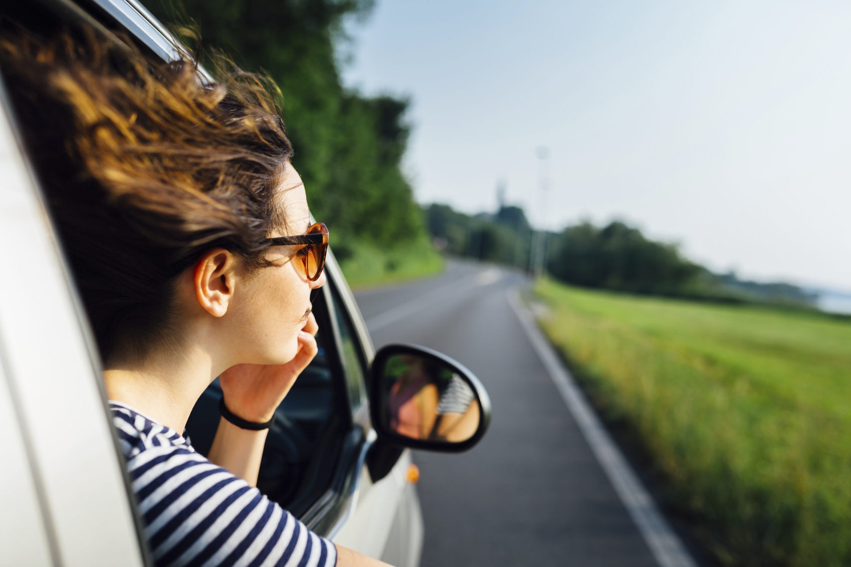 A young woman looking out the window of the car with the wind in her hair