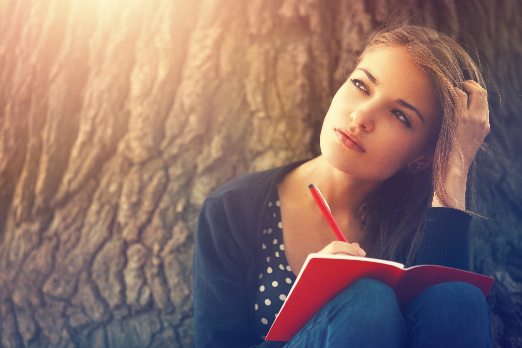 Young woman writing her journal at a tree