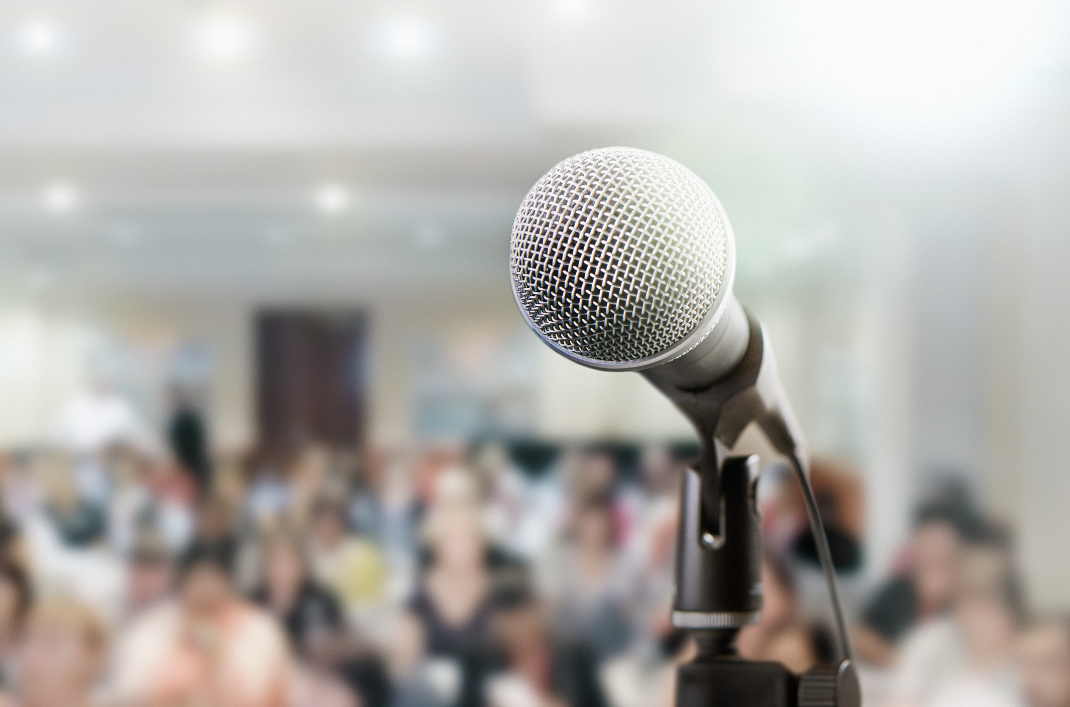 Audience sits waiting for the speaker at a conference. The microphone is in the foreground.