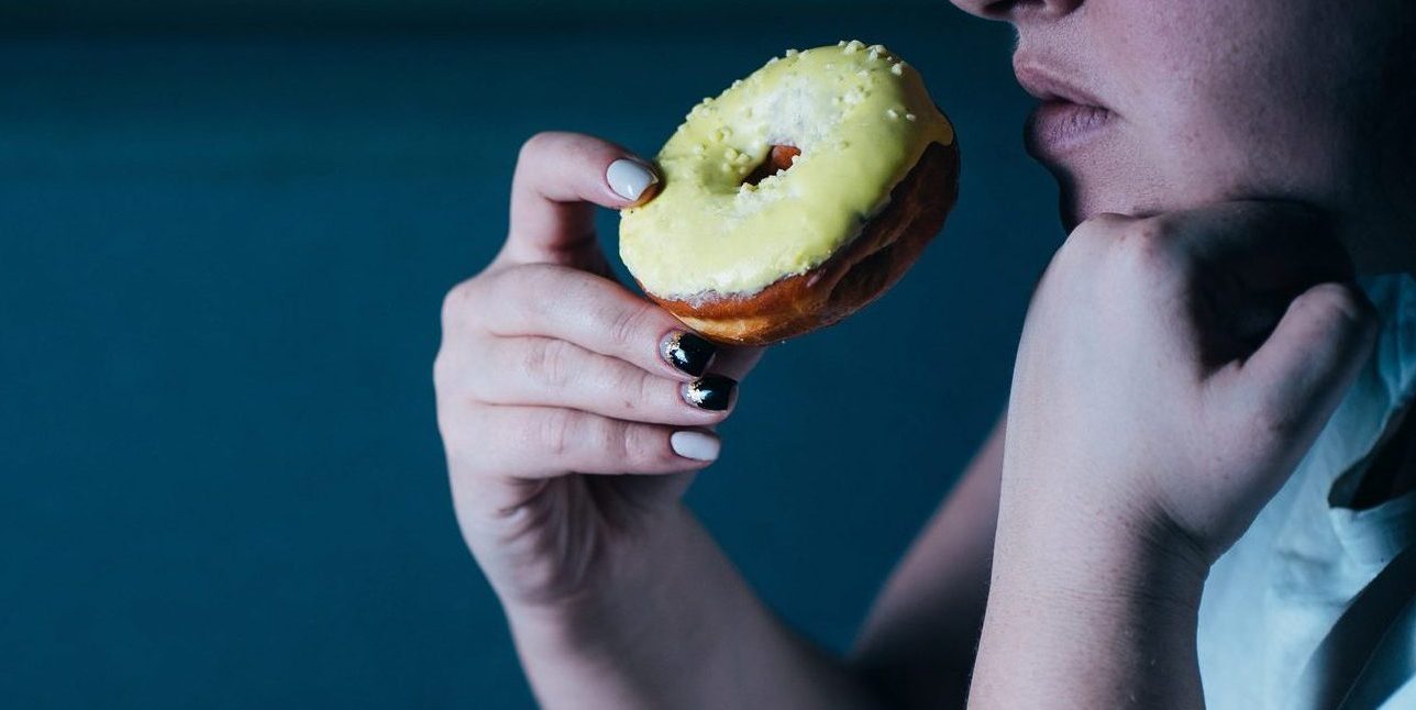 Woman laying on sofa eating sugary food