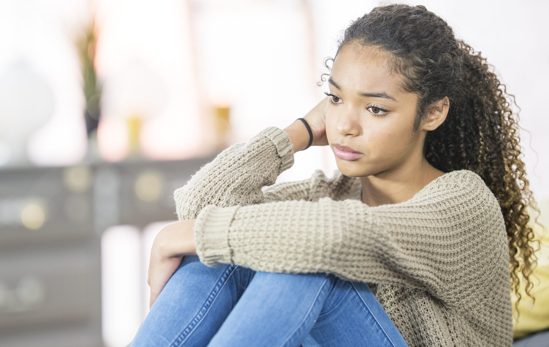 A teenage girl of African descent is indoors in a bedroom