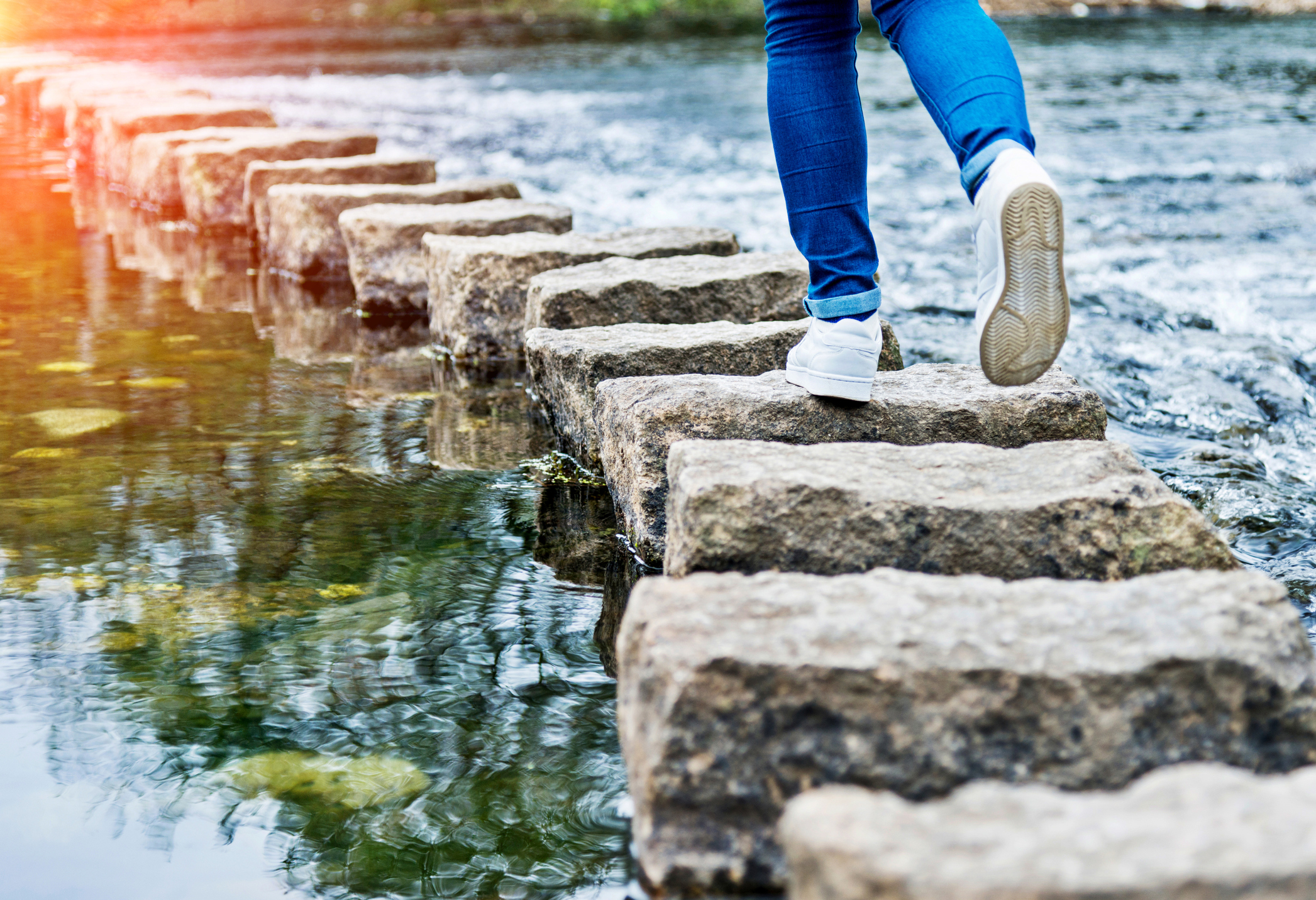 Woman paying close attention while crossing stepping stones on a river
