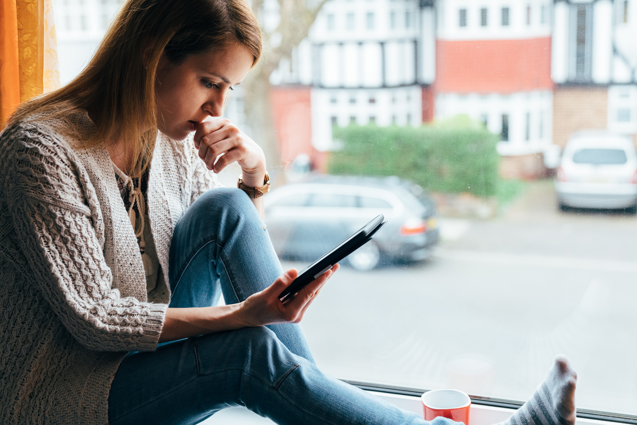 Woman looking at tablet, sitting in window