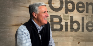 Pastor Colin smiling in front of a wooden background that says "Open the Bible"